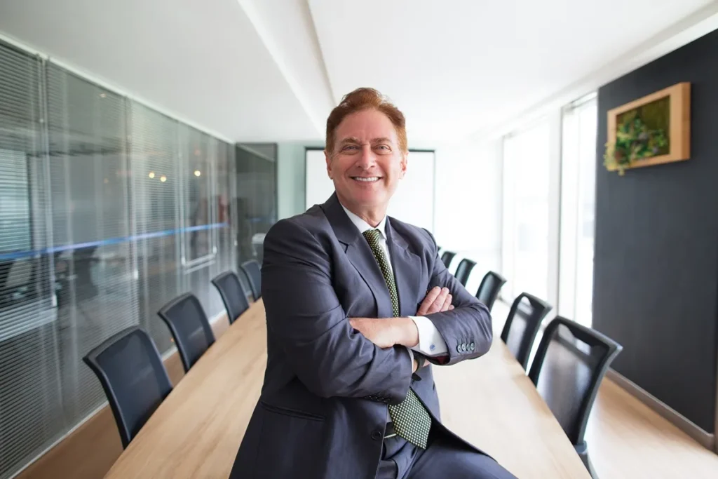 Homem de terno (CEOs) sorrindo com os braços cruzados em uma sala de reuniões moderna e iluminada