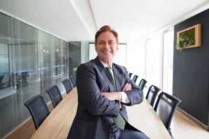 Homem de terno (CEOs) sorrindo com os braços cruzados em uma sala de reuniões moderna e iluminada
