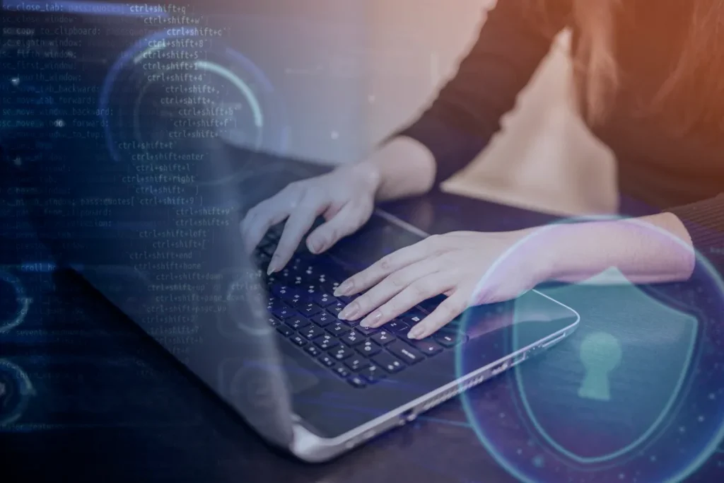 Mãos de uma pessoa digitando em um laptop com sobreposição de elementos gráficos relacionados à segurança cibernética, como cadeado e códigos.