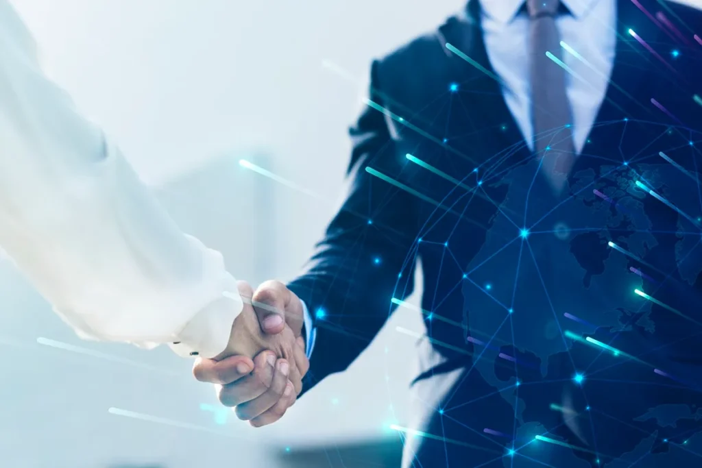 Aperto de mãos entre profissionais em terno, com gráficos digitais e representação de um globo ao fundo, simbolizando parceria e networking global.