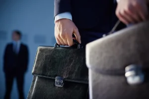 Close-up de uma mão masculina segurando uma pasta executiva de couro preta, representando negócios e formalidade no mercado corporativo