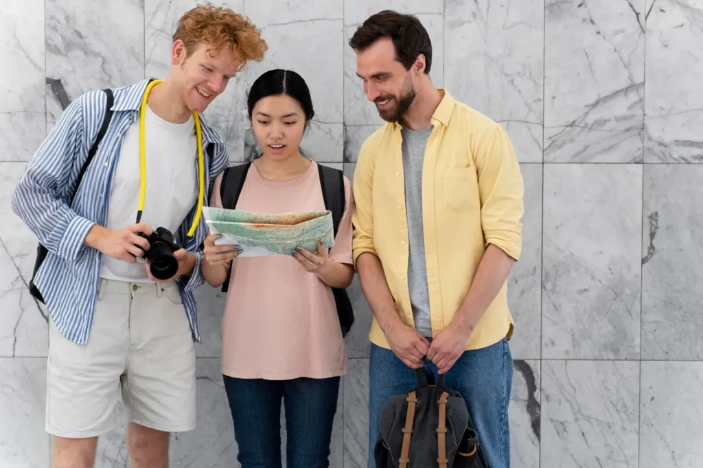 Três turistas sorridentes observando um mapa em frente a uma parede de mármore, simbolizando planejamento e guia de viagem