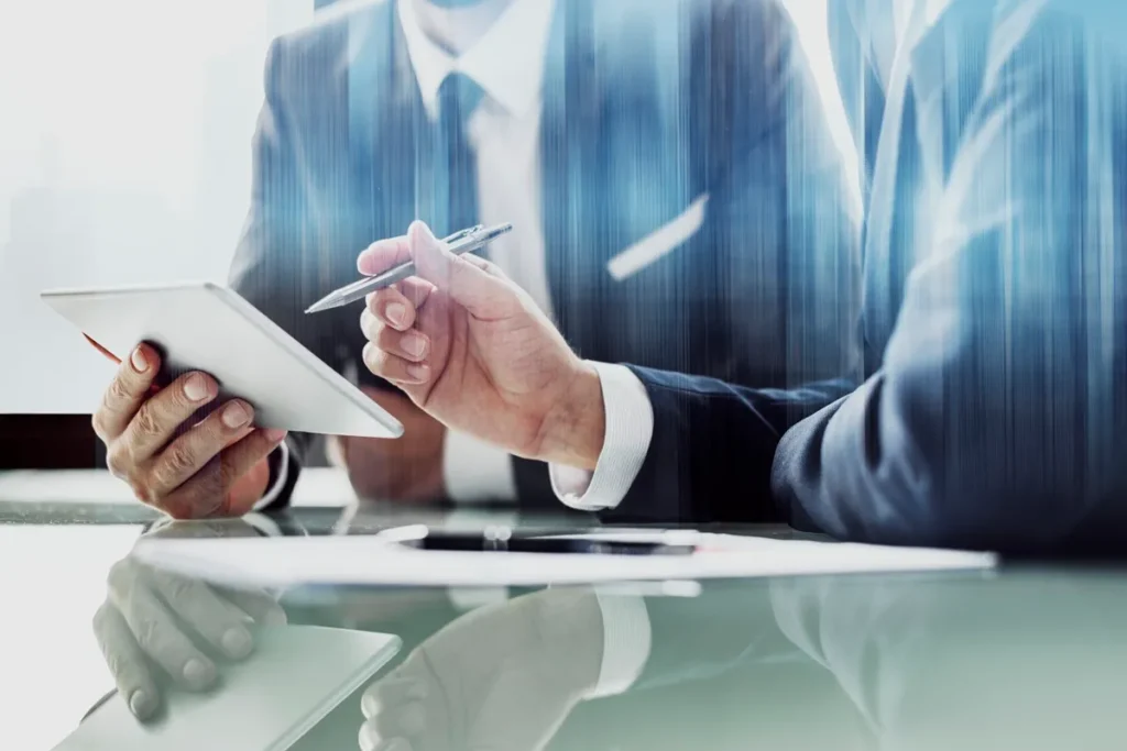 Duas pessoas em trajes formais discutindo dados em um tablet em ambiente corporativo