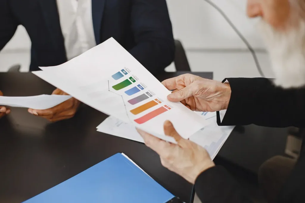 Profissionais em reunião analisando relatórios com gráficos coloridos, representando desempenho e planejamento estratégico.