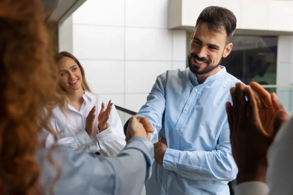 Funcionário sendo reconhecido com um aperto de mão e aplausos em uma reunião de equipe.