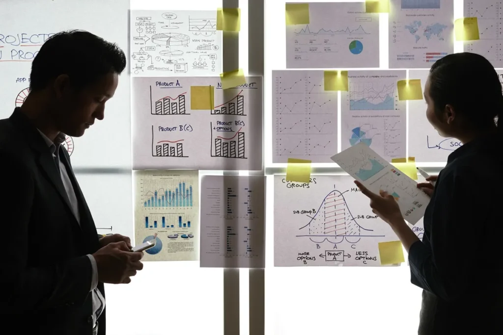 Duas pessoas analisando gráficos e planos estratégicos em um quadro iluminado, destacando dados de gerenciamento de projetos.