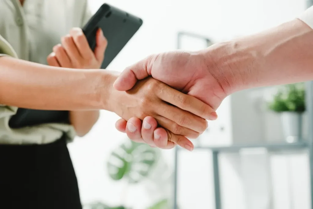 Duas pessoas apertando as mãos em um ambiente corporativo, simbolizando confiança e estabelecimento de uma parceria profissional.