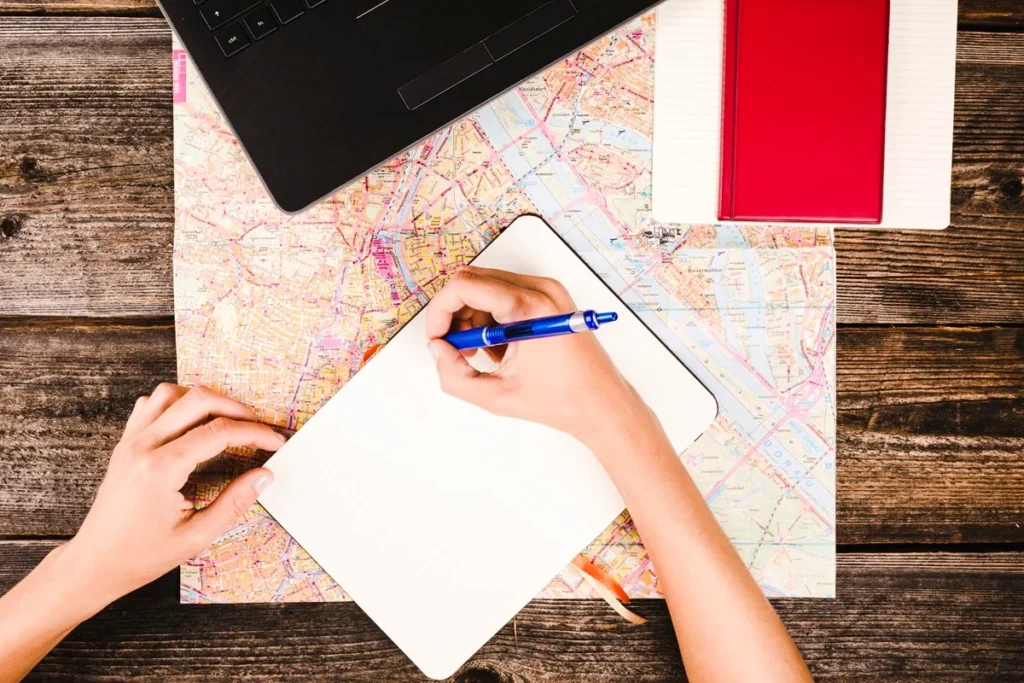 Pessoa escrevendo em caderno sobre um mapa, simbolizando planejamento de viagem detalhado