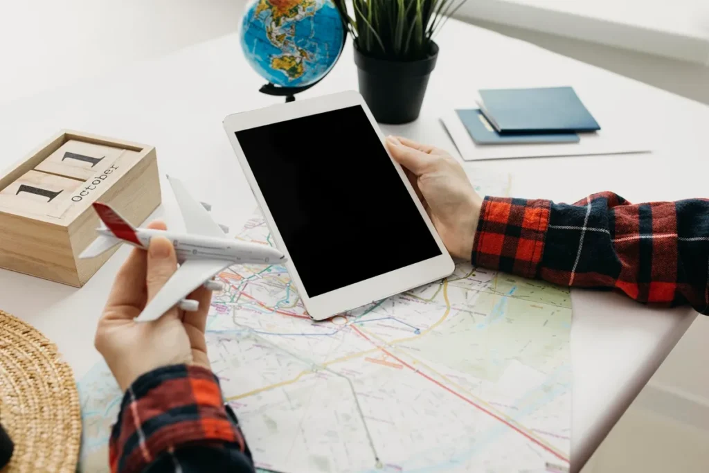 Pessoa segurando um tablet e um avião em miniatura sobre um mapa, representando planejamento de viagem com tecnologia