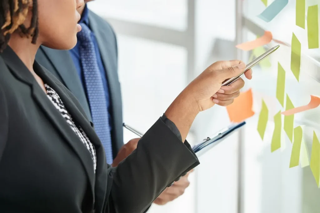 Profissionais analisando notas em post-its coloridos durante uma reunião de planejamento estratégico em um ambiente corporativo.
