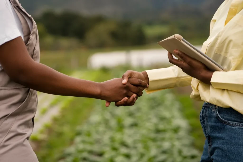 Duas pessoas apertando as mãos em um campo agrícola, simbolizando parceria, confiança e negociação no agronegócio.