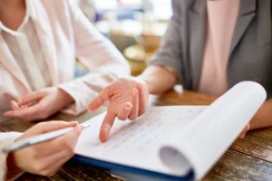 Duas pessoas analisando documentos e discutindo detalhes de uma proposta em um ambiente de trabalho colaborativo.