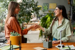 Duas mulheres apertando as mãos em um ambiente repleto de plantas, representando relações sustentáveis e parcerias ecológicas.