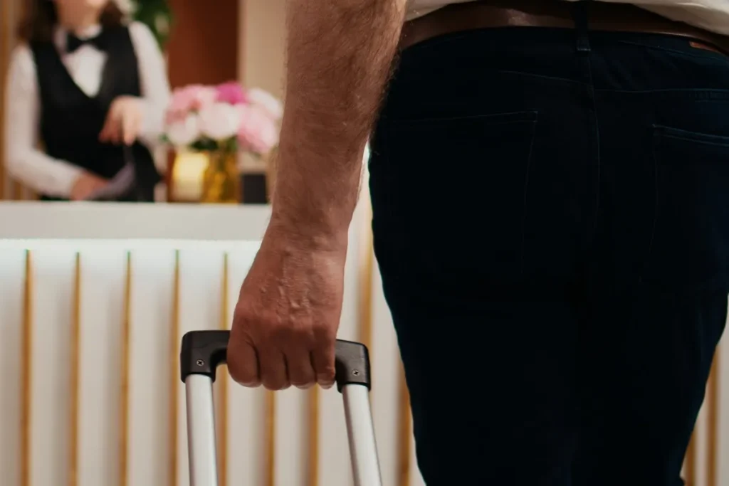 Pessoa segurando uma mala durante o check-in em um hotel, com recepcionista ao fundo no balcão