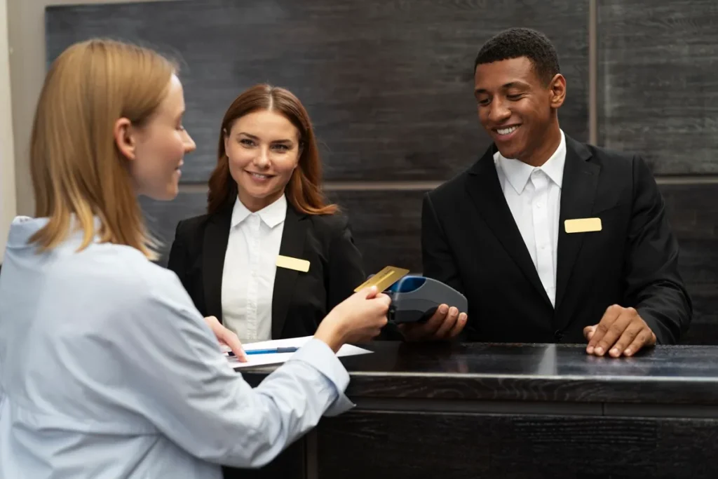Recepcionistas de hotel sorrindo enquanto processam o pagamento de uma hóspede no balcão de check-in