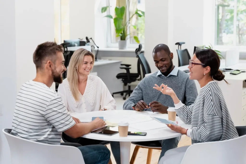 Equipe diversa em uma reunião colaborativa ao redor de uma mesa redonda em um ambiente corporativo moderno e iluminado.