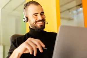 Homem sorridente usando headset enquanto trabalha no suporte técnico com um notebook.
