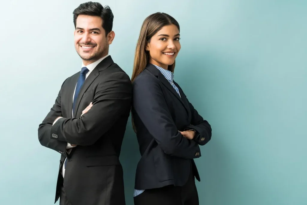 Dois profissionais sorridentes, um homem e uma mulher em trajes formais, de braços cruzados, simbolizando confiança e sucesso.