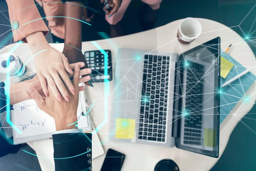 Mãos unidas em um gesto de colaboração sobre uma mesa com laptops, gráficos e café, representando a transformação digital e inovação nos negócios.
