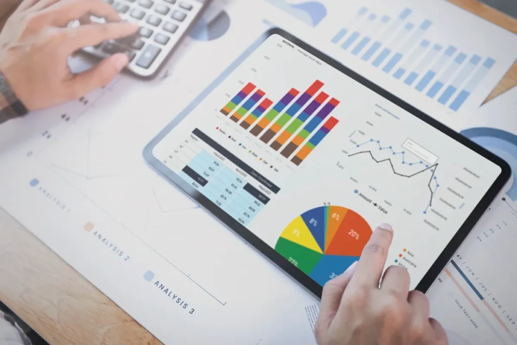 Tablet exibindo gráficos coloridos e relatórios financeiros, enquanto um profissional analisa dados e digita em uma calculadora.