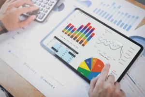 Tablet exibindo gráficos coloridos e relatórios financeiros, enquanto um profissional analisa dados e digita em uma calculadora.