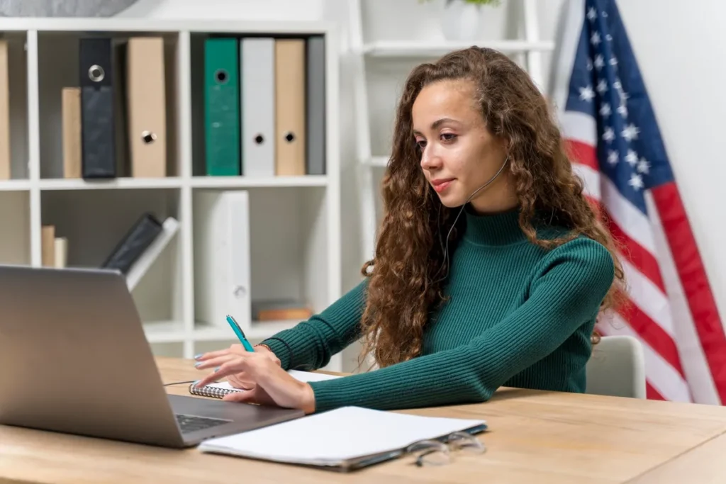 Jovem estudando inglês online, usando fones de ouvido e laptop, com a bandeira dos Estados Unidos ao fundo.