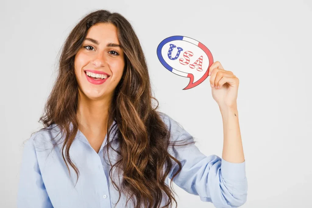 Mulher sorridente segurando um balão de fala com a palavra "USA" e as cores da bandeira americana, simbolizando o aprendizado de inglês.