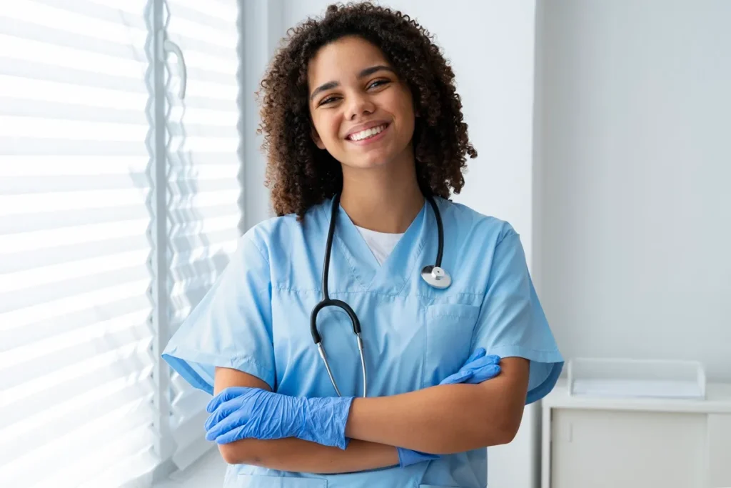 Enfermeira sorridente vestindo uniforme azul, luvas descartáveis e estetoscópio, transmitindo confiança e simpatia.
