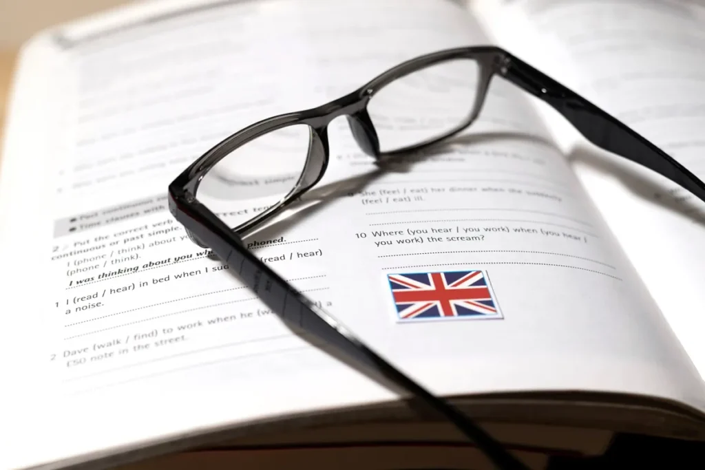 Livro de exercícios de inglês técnico com óculos de grau apoiados sobre a página e bandeira do Reino Unido impressa.