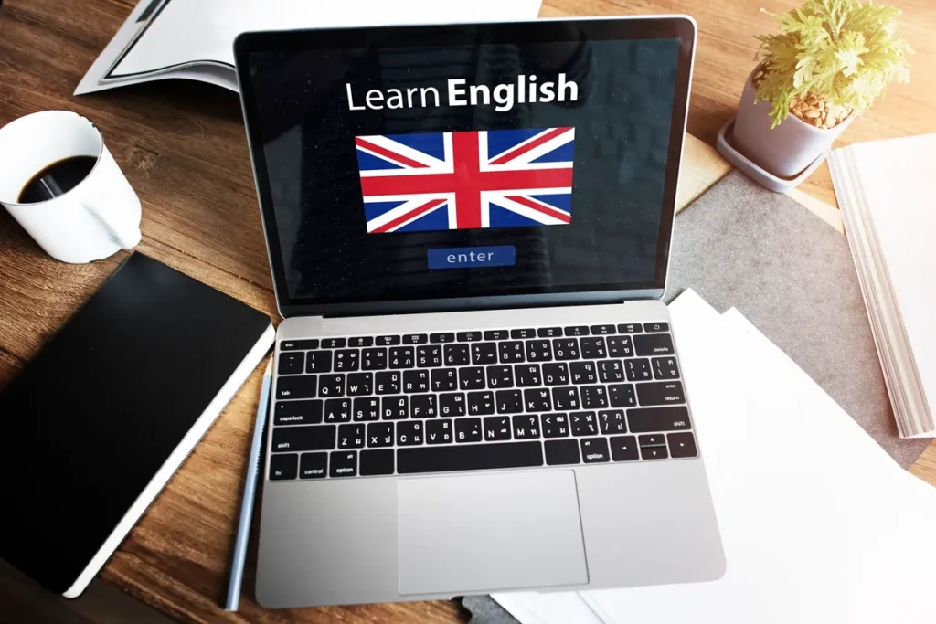 Notebook sobre mesa com a tela exibindo "Learn English" e bandeira do Reino Unido, indicando plataforma de estudo de inglês online.