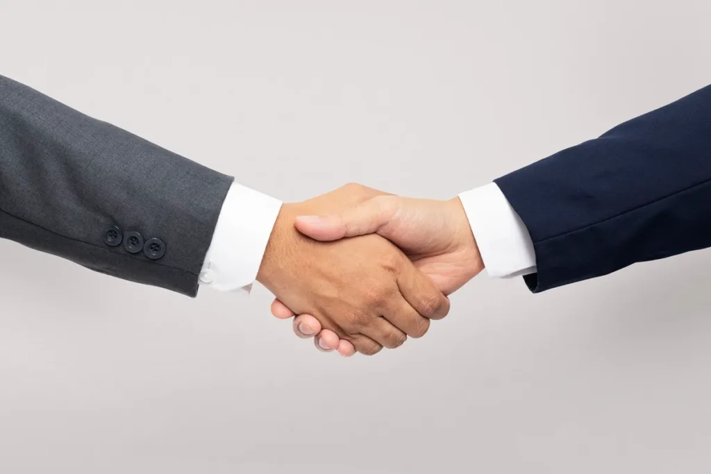 Aperto de mãos entre duas pessoas usando ternos formais, simbolizando parceria profissional.
