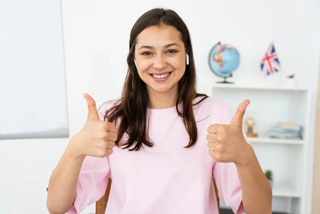 Mulher sorridente mostrando sinal de positivo com as duas mãos, simbolizando aprovação e confiança no aprendizado de inglês.