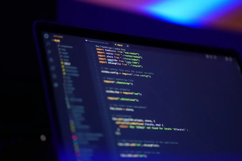  Uma tela de laptop com um editor de texto exibindo linhas de código de programação em JavaScript e PHP, em um ambiente escuro. A imagem representa o trabalho de desenvolvimento e codificação.