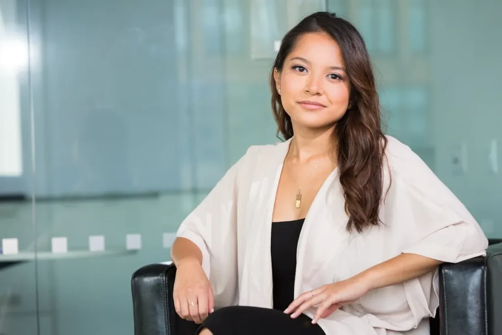 Mulher, profissional C-level, sentada em uma poltrona de escritório com olhar confiante. A imagem transmite profissionalismo, liderança e sucesso em um ambiente corporativo.