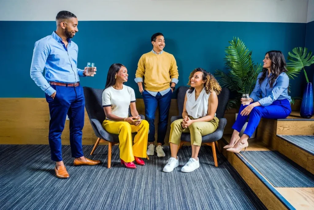Um grupo de quatro executivos C-level, sentados e em pé, conversando em um ambiente de escritório casual e moderno. A imagem representa networking, colaboração e liderança em um contexto descontraído.