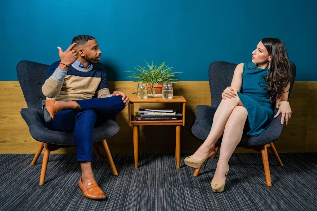Um homem e uma mulher, ambos profissionais C-level, sentados em poltronas, engajados em uma conversa séria em um ambiente de escritório. A imagem transmite diálogo, consultoria, e colaboração de alto nível.