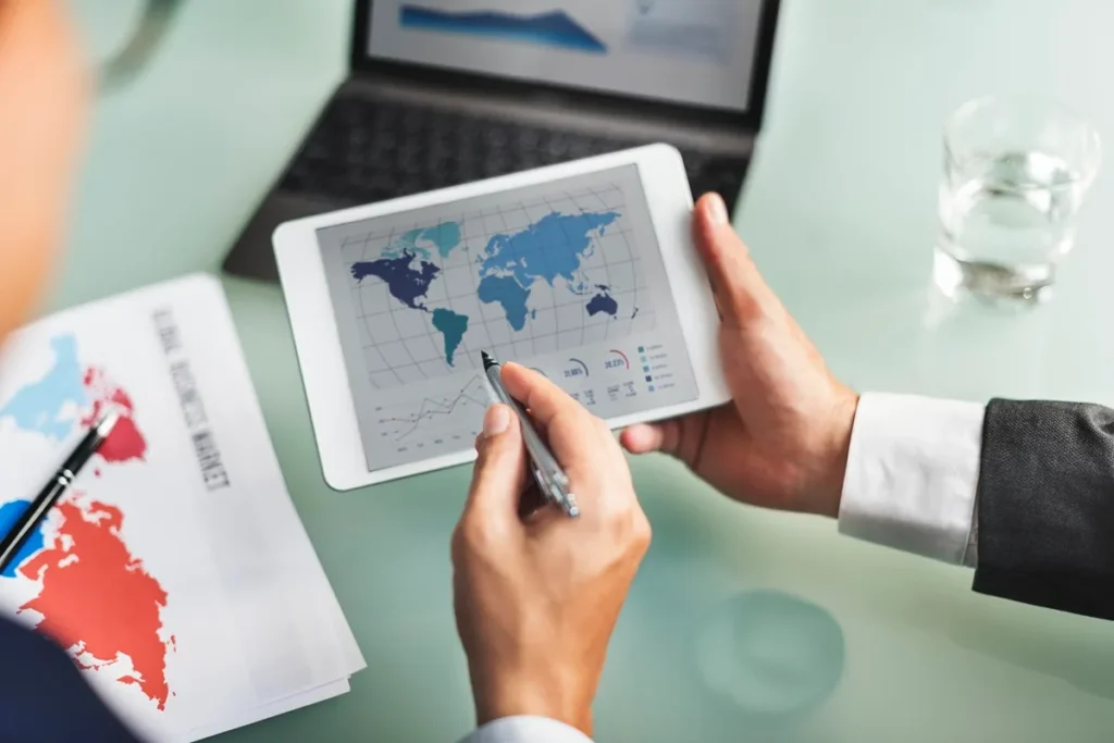 Imagem de uma análise de mercado global com gráficos em um tablet, enquanto um executivo observa e faz anotações em um relatório impresso.