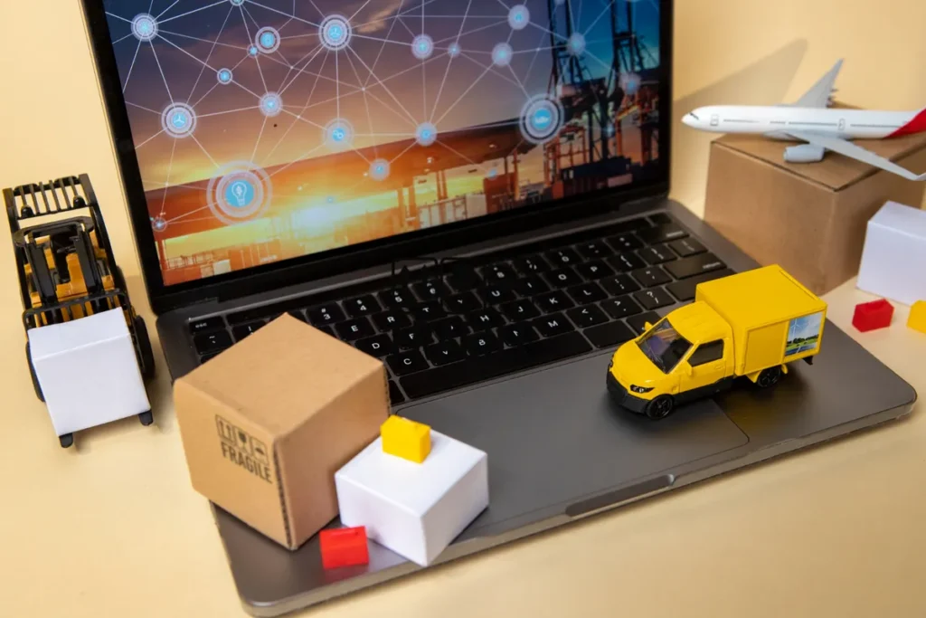 Miniaturas de caminhão e avião em um notebook com imagem de um porto de contêineres na tela. A imagem representa o comércio exterior, logística, transporte e a tecnologia.