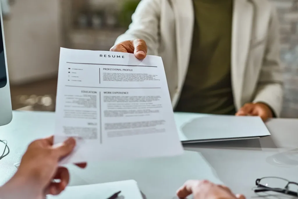 Imagem de um profissional entregando seu currículo em uma entrevista de emprego, com destaque para a seção de 'Perfil Profissional' e 'Experiência de Trabalho'. A cena transmite um momento importante de um processo seletivo