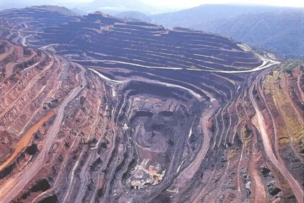 Vista aérea de uma gigantesca mina a céu aberto, com estradas em espiral descendo para o centro da escavação.