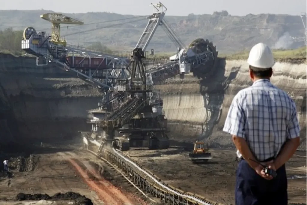 Um engenheiro de mineração com capacete e colete de segurança, observando uma escavadeira gigante em uma mina.