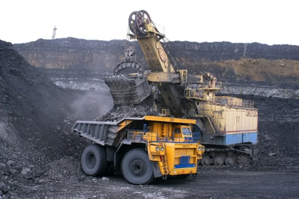 Escavadeira industrial de grande porte carregando minério em um caminhão de mineração em uma mina a céu aberto.