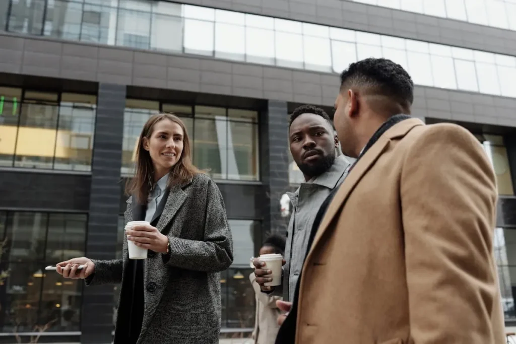 Executivos de uma multinacional em conversa casual na rua, com xícaras de café em mãos.