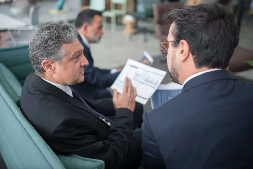 Executivos de uma multinacional em uma reunião informal, discutindo gráficos e relatórios financeiros, sentados em um sofá.