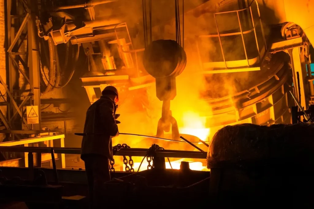 Trabalhador com capacete em uma siderúrgica com forno de aço incandescente.