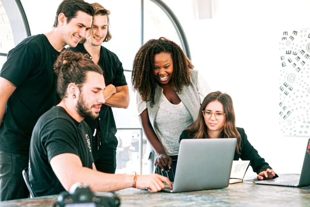  Uma equipe diversa de quatro jovens em uma startup, colaborando ao redor de um laptop. A imagem representa inovação, trabalho em equipe e o ambiente de startups.