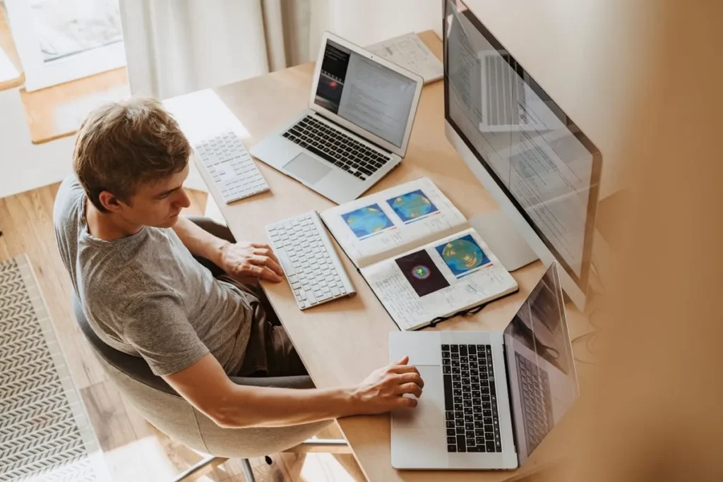 Um profissional de TI trabalhando em uma estação de trabalho com três computadores e notebooks. A imagem destaca a versatilidade, a tecnologia e o ambiente de trabalho de um profissional de TI.