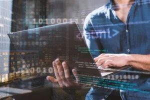 Programador de camisa azul digitando em um laptop enquanto código binário e informações digitais são exibidas ao fundo, com vista para prédios urbanos.