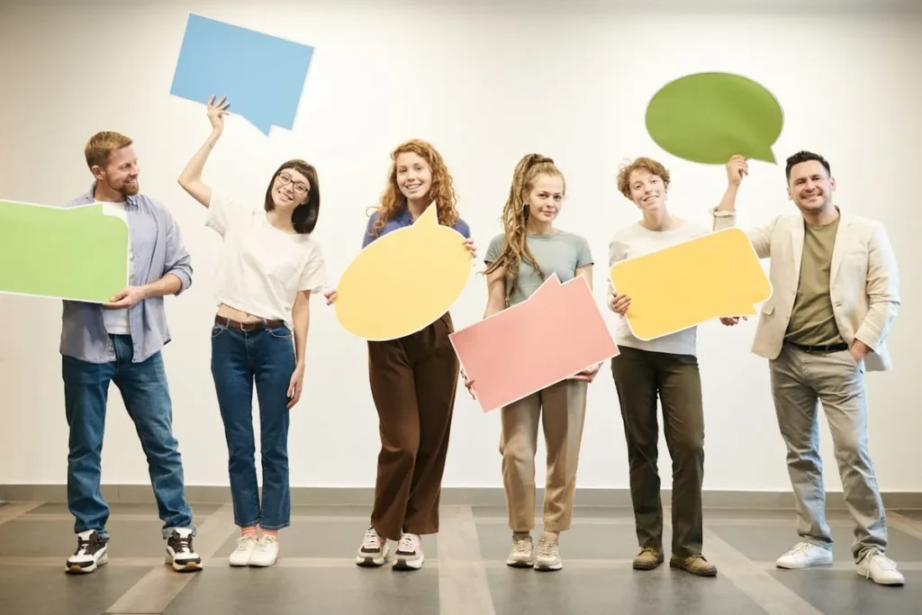 Grupo diverso de pessoas segurando balões de fala coloridos, representando comunicação e aprendizado de idiomas em grupo.