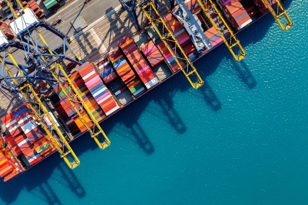 Vista aérea de um porto de contêineres, mostrando o cais e os contêineres coloridos sendo carregados por guindastes
